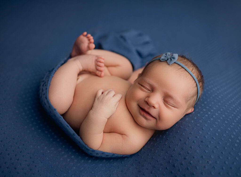Colorado Springs Newborn Photography poses baby in blue with a smile. 